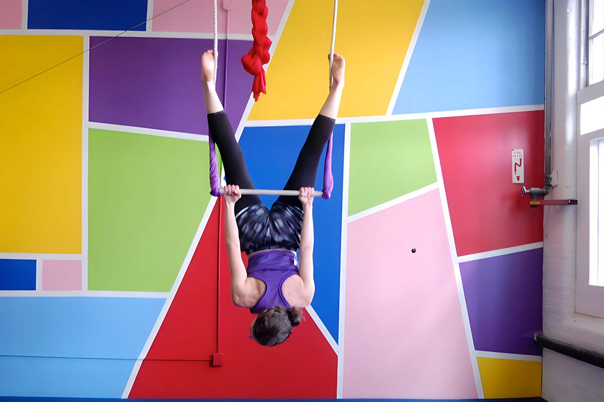 Back-view of a student hanging upside down from a trapeze at SHOW Circus Studio in Easthampton, Massachusetts