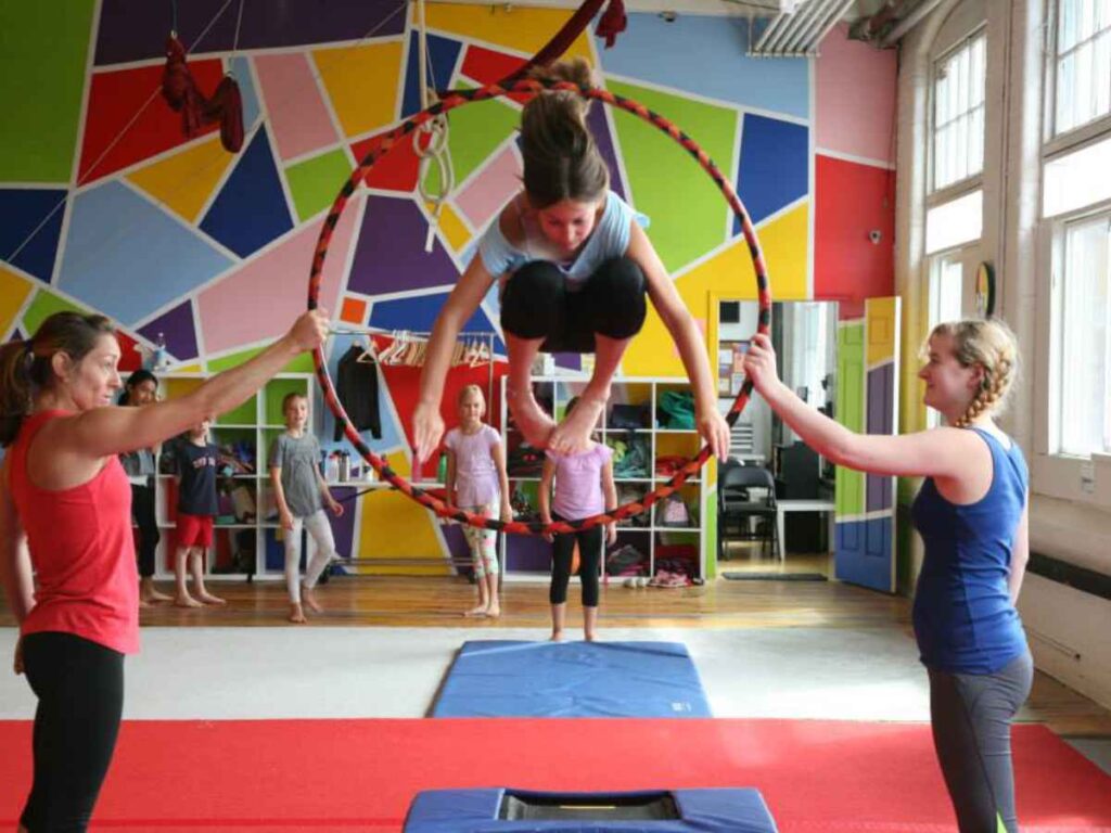 A kid using a mini-tramp to jump through a hoop held by two instructors at SHOW Circus Studio in Easthampton, Massachusetts